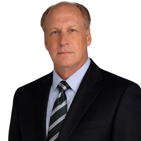 Professional headshot of a middle-aged man in a black blazer, light blue dress shirt, and striped tie against a white background